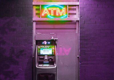 An ATM lit up at night against a purple brick wall